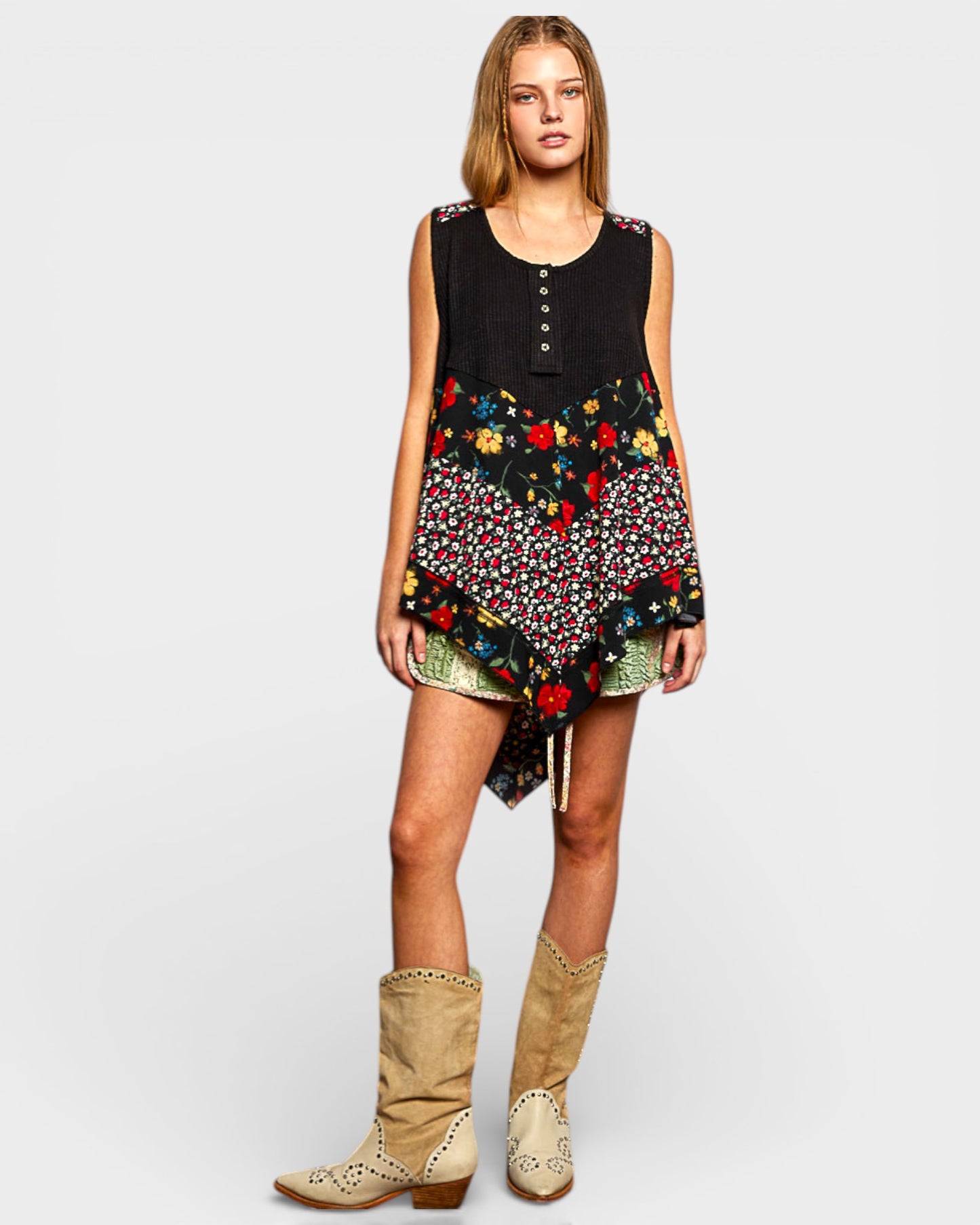 Woman wearing a black sleeveless top with floral patterns and beige cowboy boots on a white background