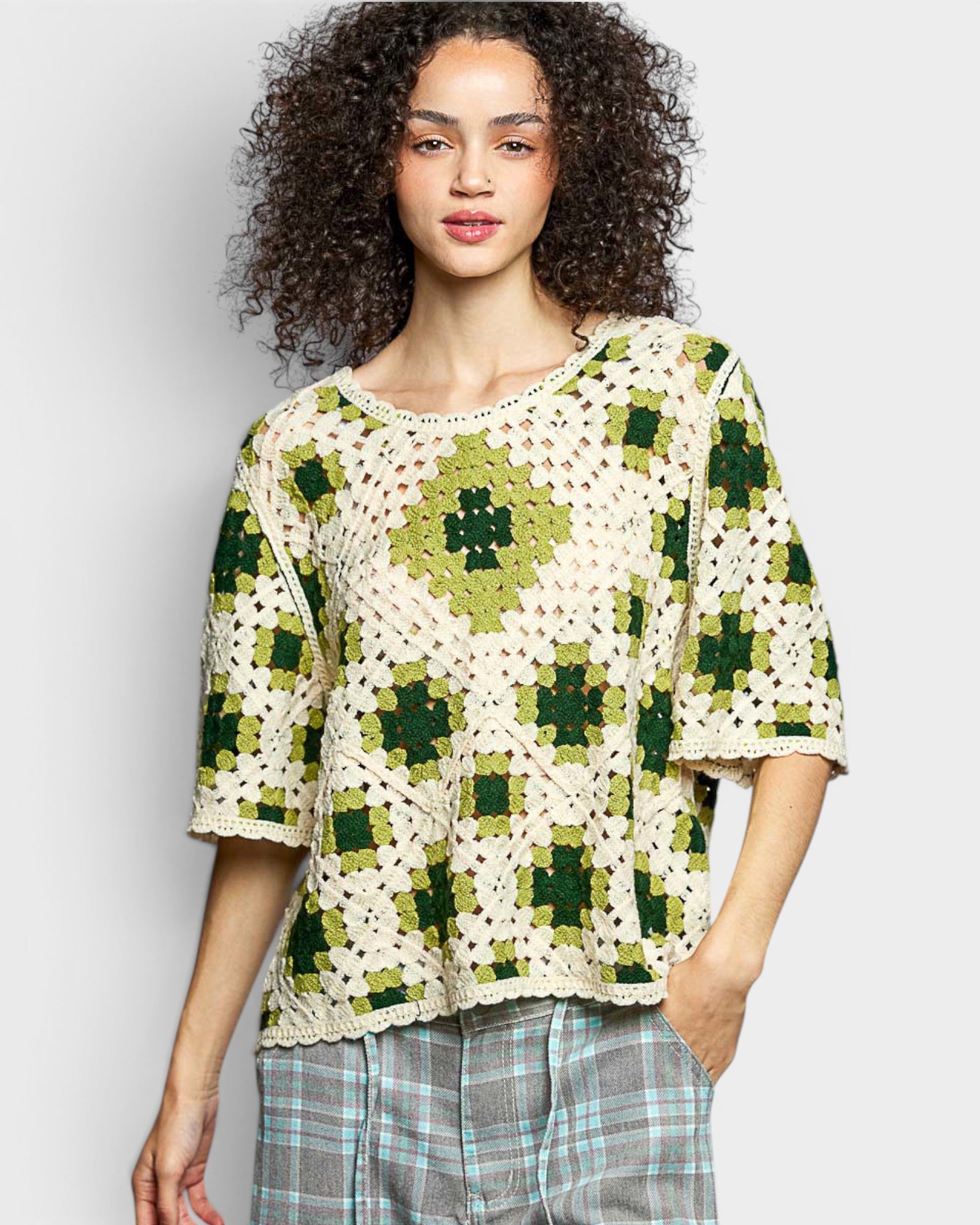 Woman wearing a green and white crochet top against a plain background