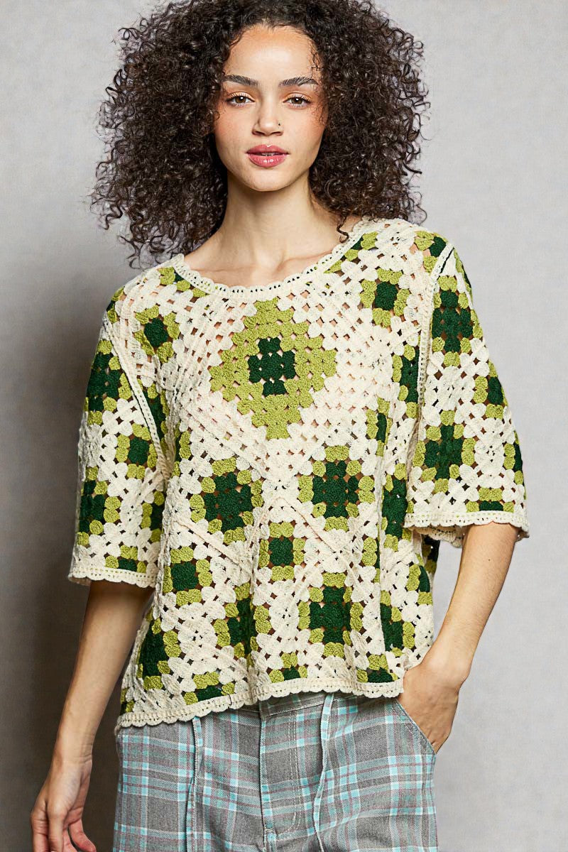 Woman wearing a green and white crochet top against a gray background