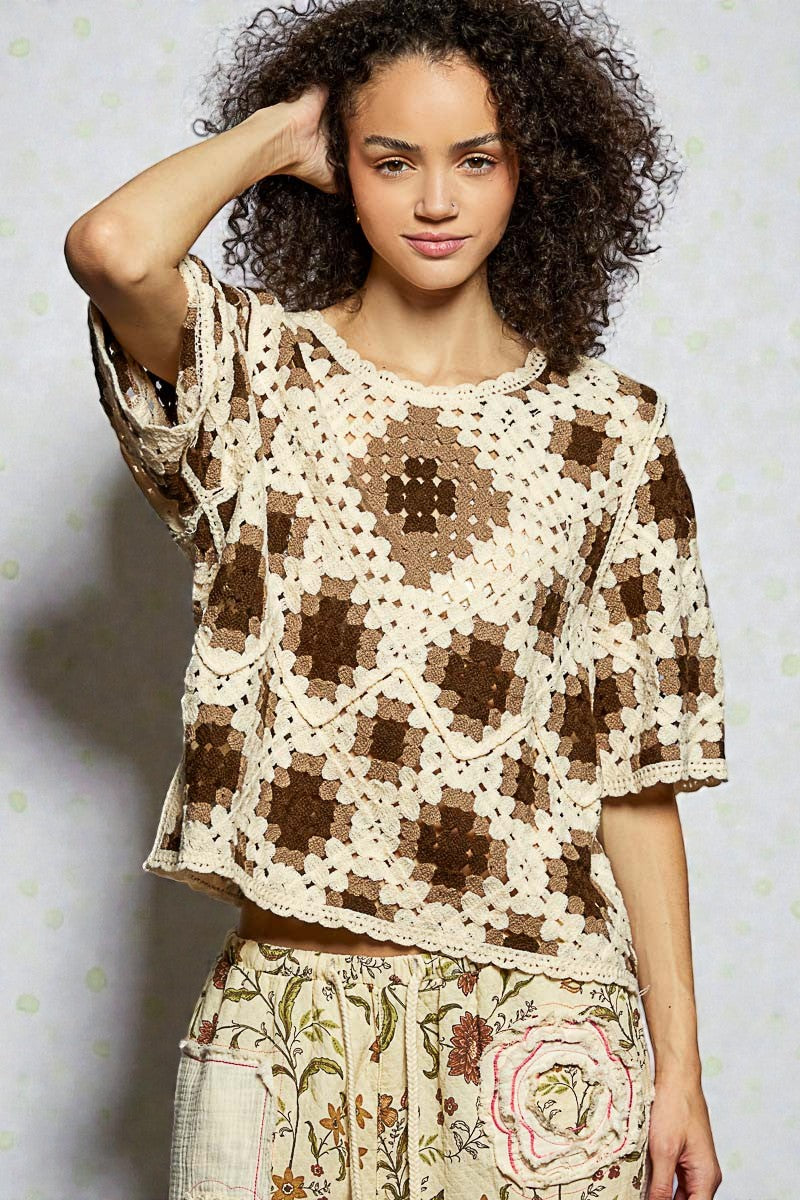 Woman wearing a brown and beige crochet top with floral pants against a light background