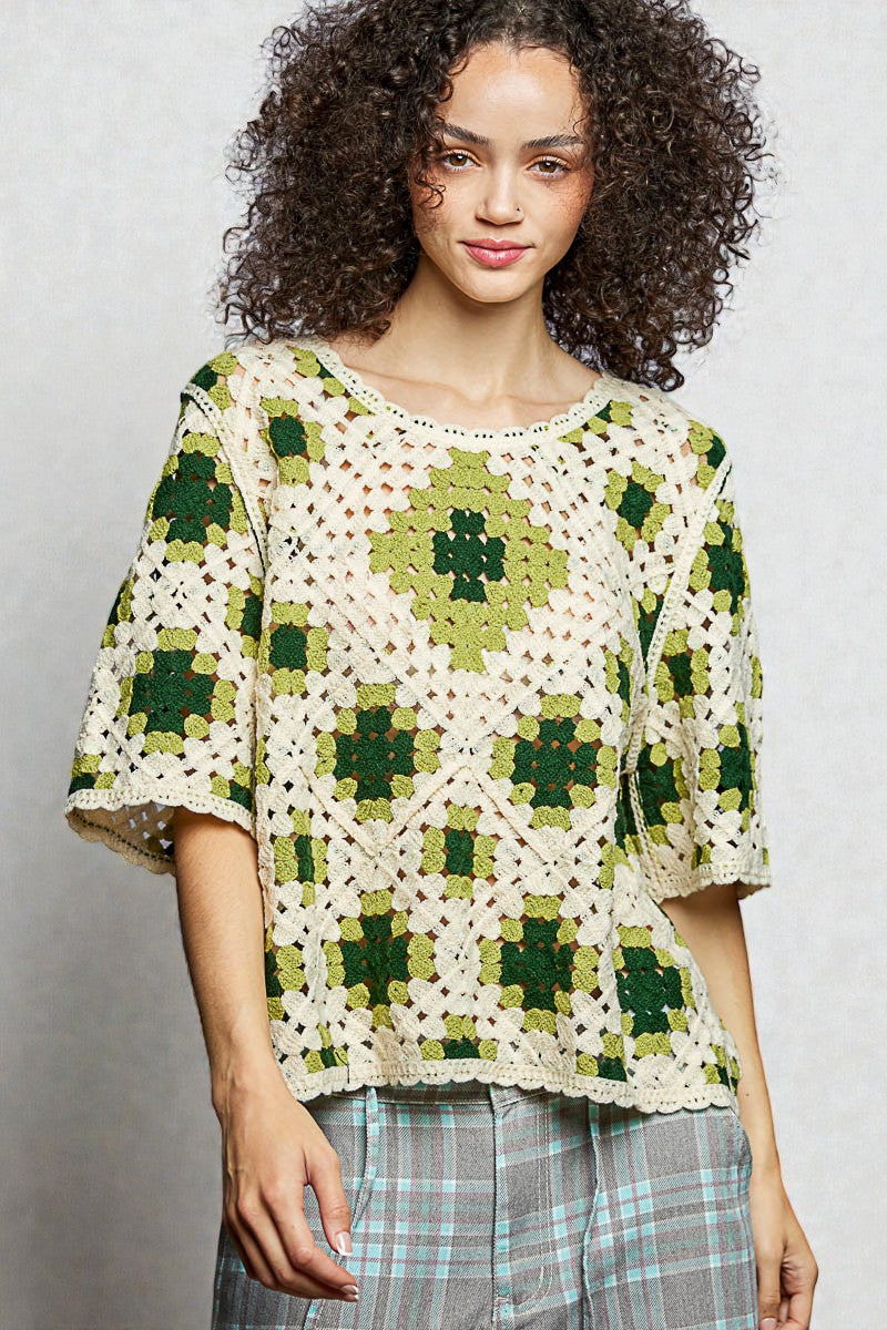 Woman wearing a green and white crocheted top against a plain background
