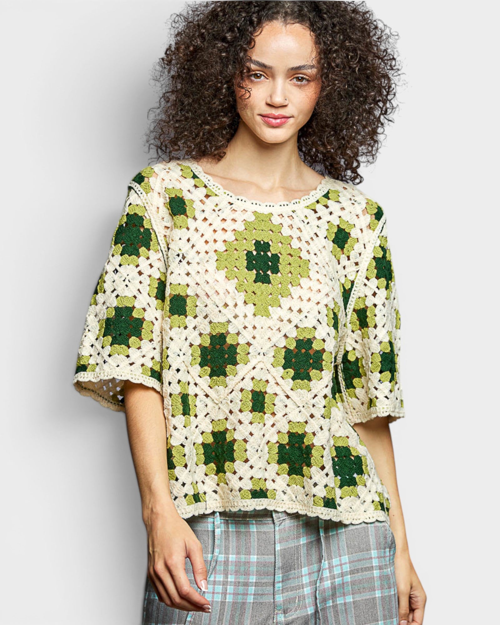 Woman wearing a green and white crochet top against a plain background