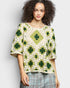 Woman wearing a green and white crochet top against a plain background