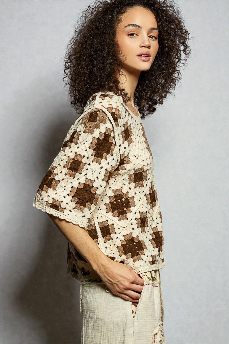 Woman wearing a crocheted brown and beige patterned top against a gray background