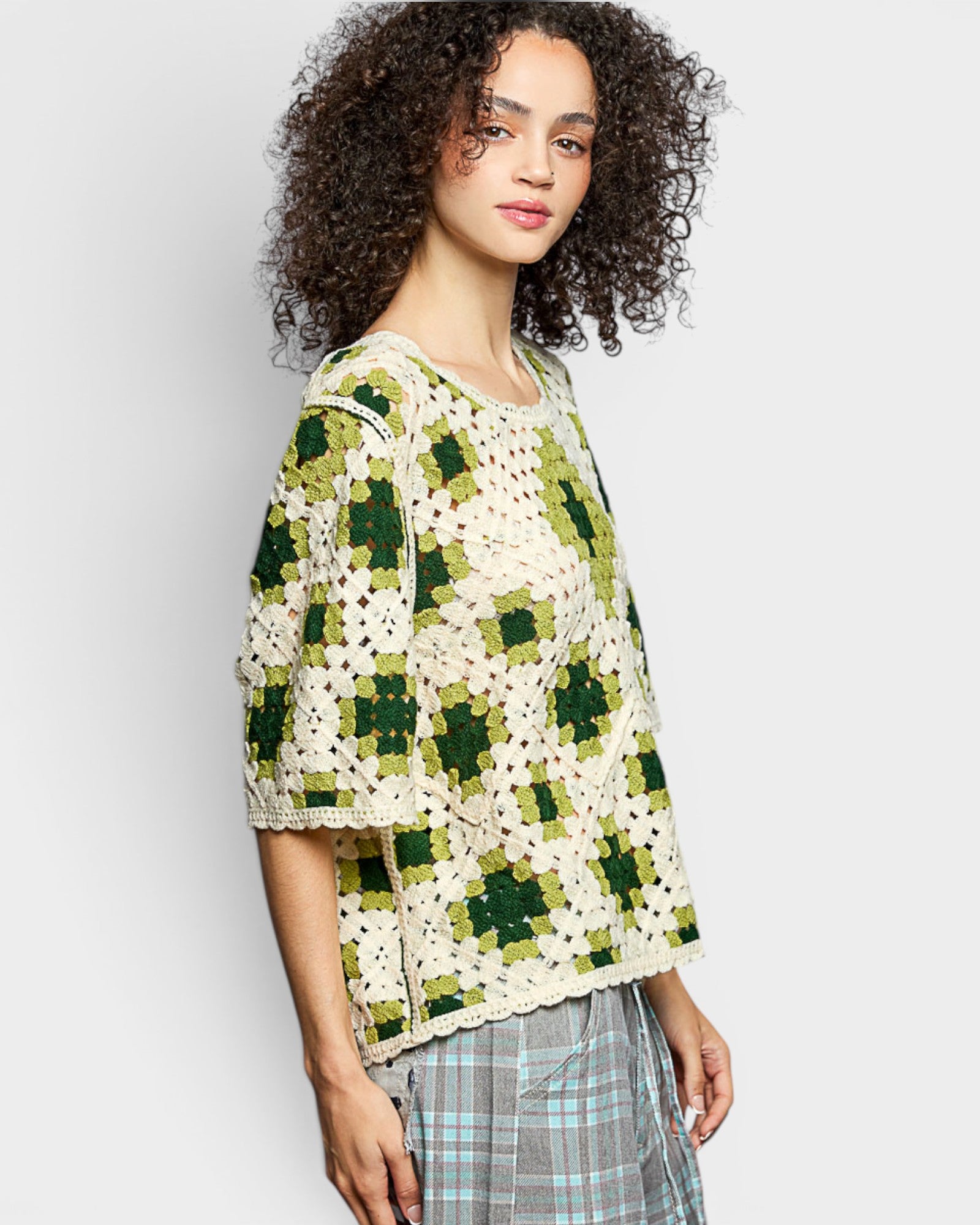 Woman wearing a green and white patterned crochet cardigan on a plain background