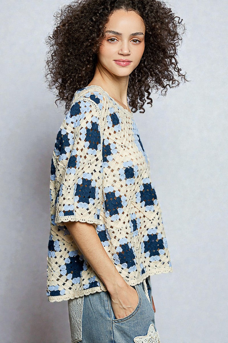 Woman wearing a colorful crochet top against a plain background