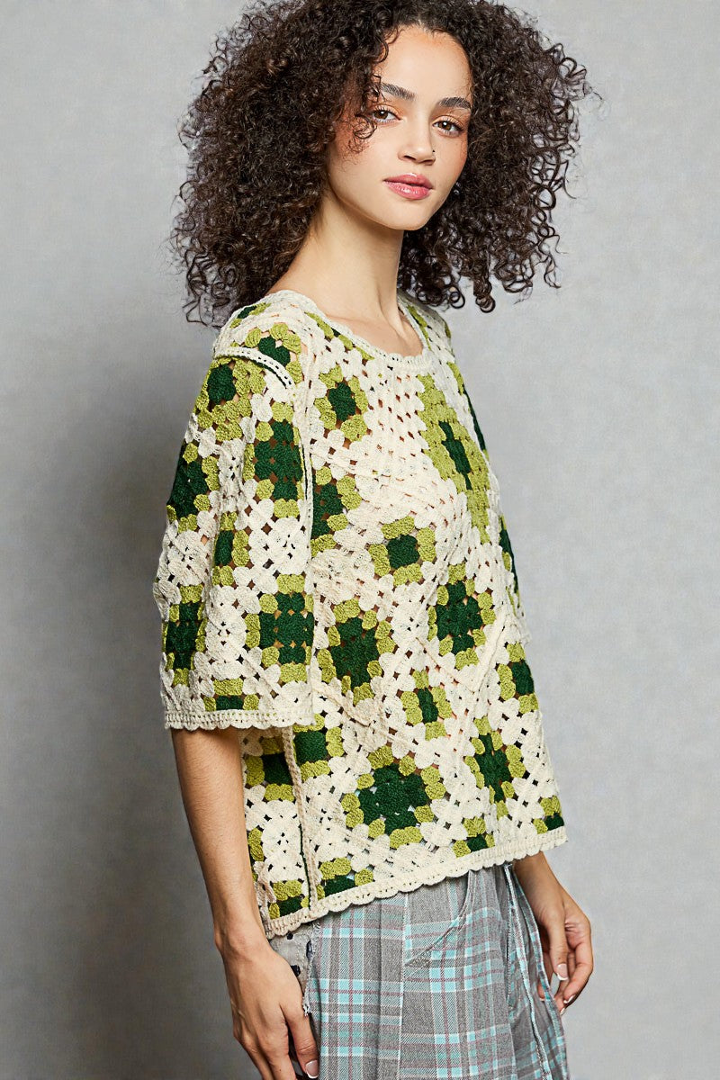 Woman wearing a green and white crocheted cardigan against a gray background