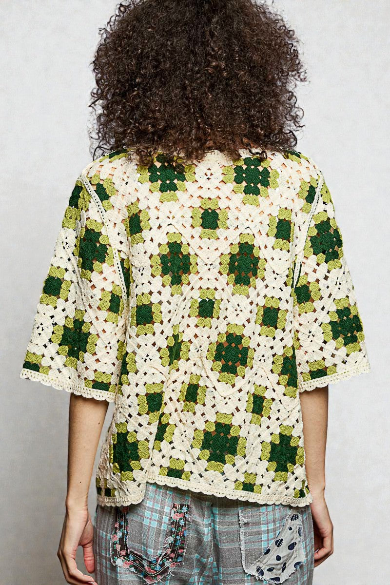 Person wearing a green and white crocheted top with a plain background