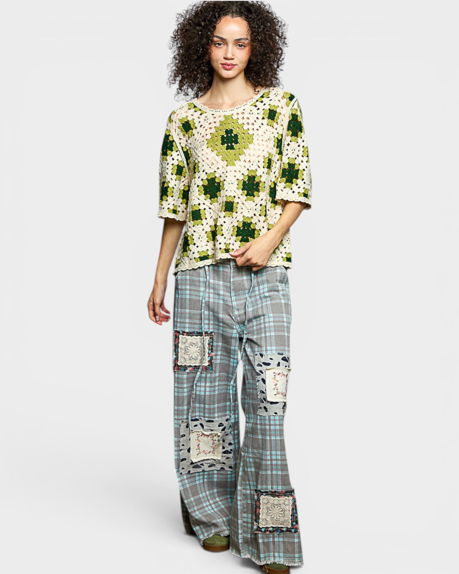 Woman wearing a patterned top and plaid pants with patches on a white background