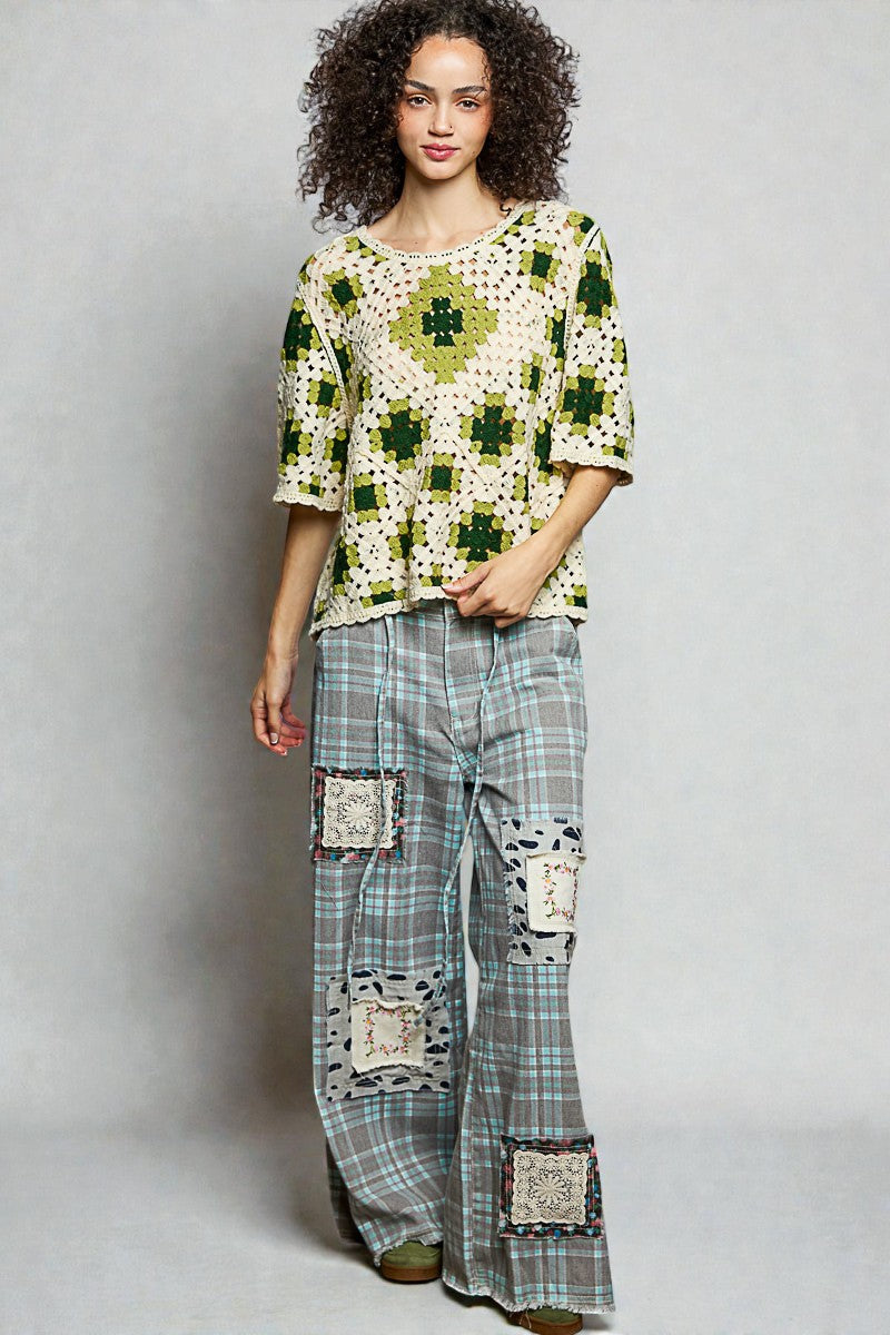 Woman wearing a patterned top and plaid pants with patches on a gray background