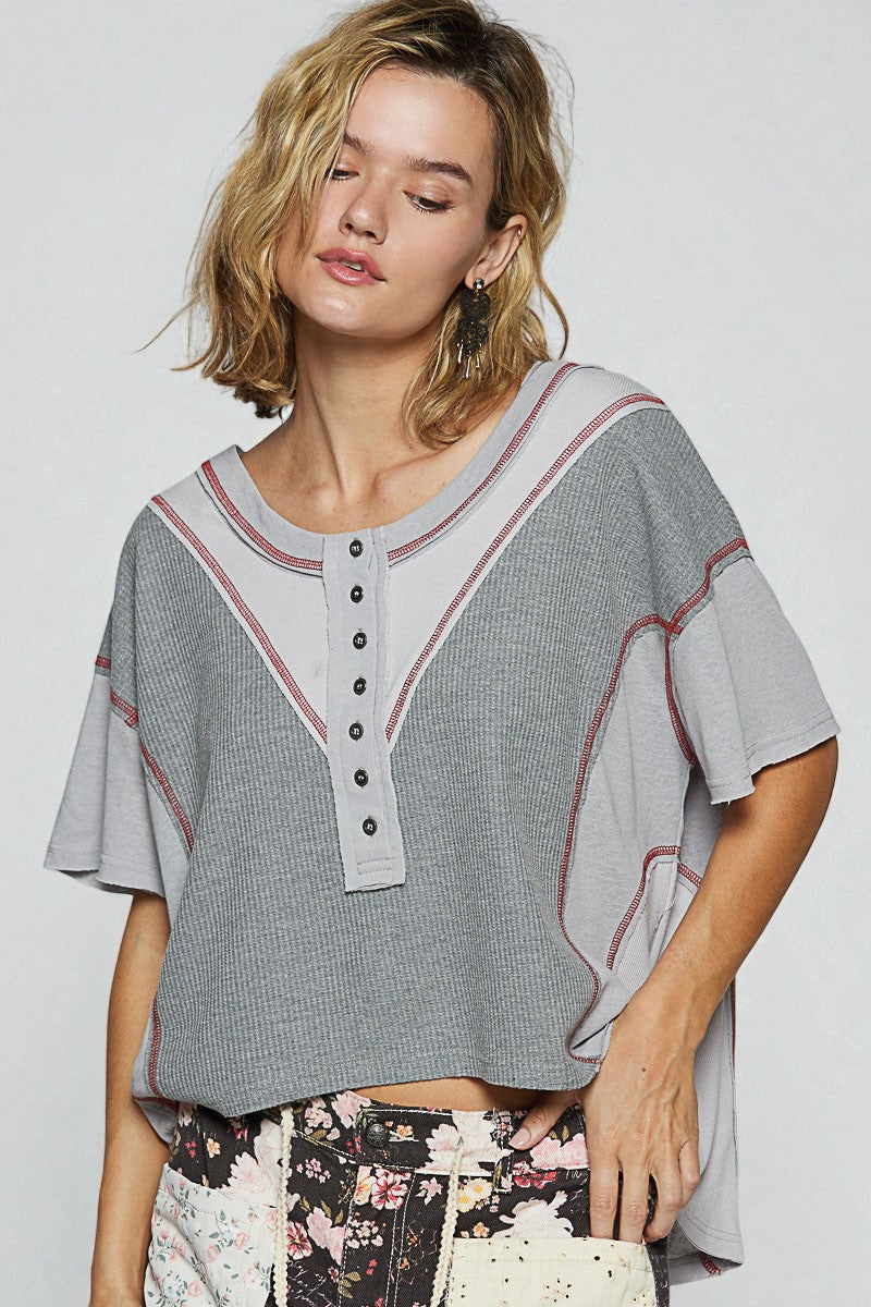 Woman wearing a gray patterned top with black buttons on a white background