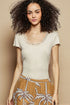 Woman wearing a beige top with lace trim and a patterned skirt against a beige background