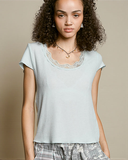 Woman wearing a light blue top with lace trim against a beige background