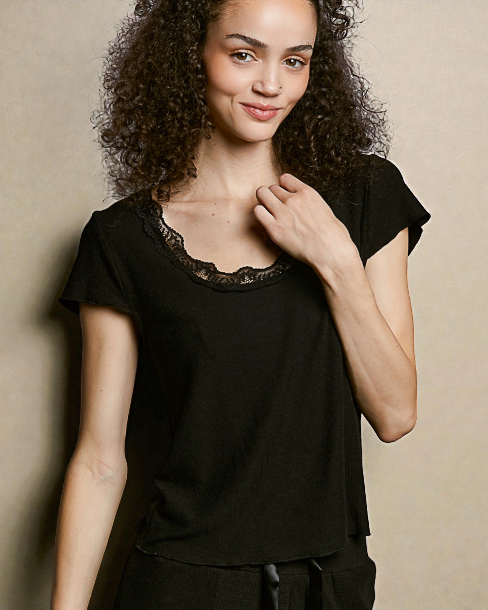 Woman wearing a black top with lace neckline against a beige background