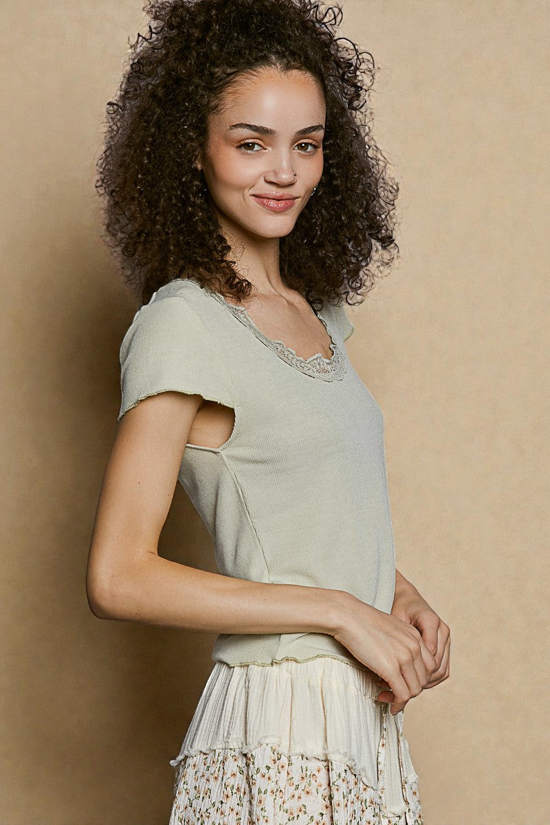 Woman wearing a light green top with lace details against a beige background