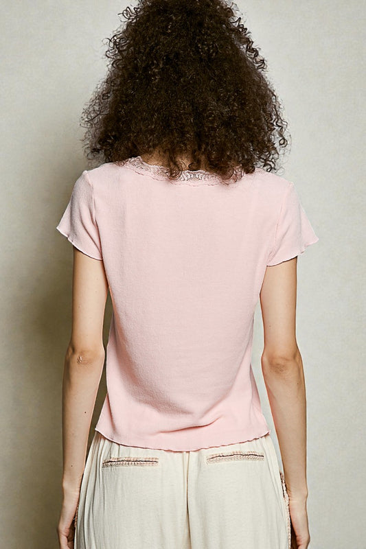 Person wearing a light pink t-shirt with lace trim on a plain background