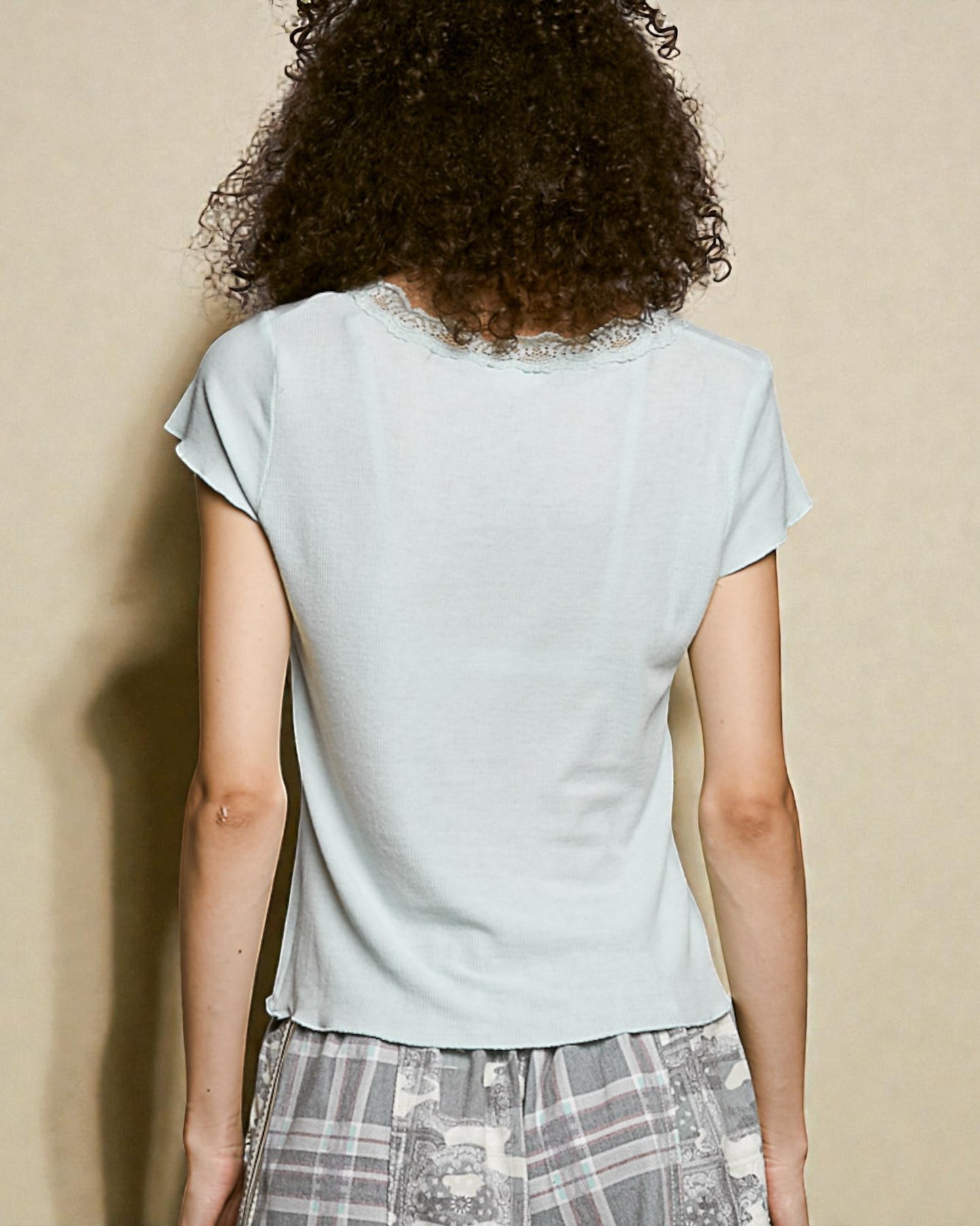 Person wearing a light blue top with lace trim on a beige background