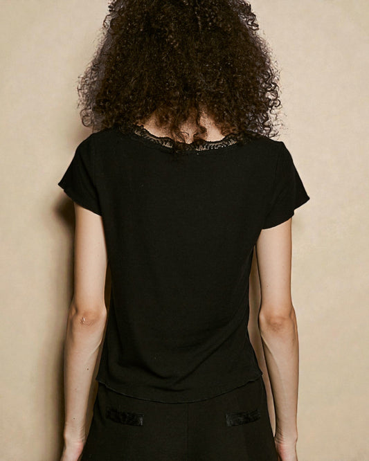 Person wearing a black top with lace details against a beige background