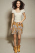 Woman wearing a white top and patterned skirt with boots against a plain background