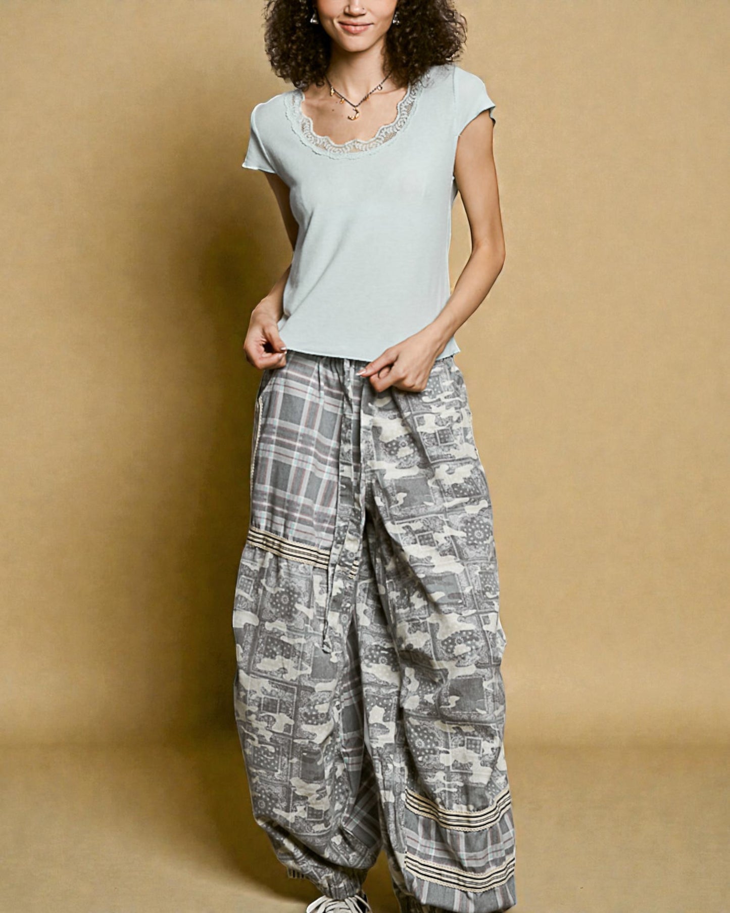 Woman wearing a light blue top and patterned gray pants against a beige background