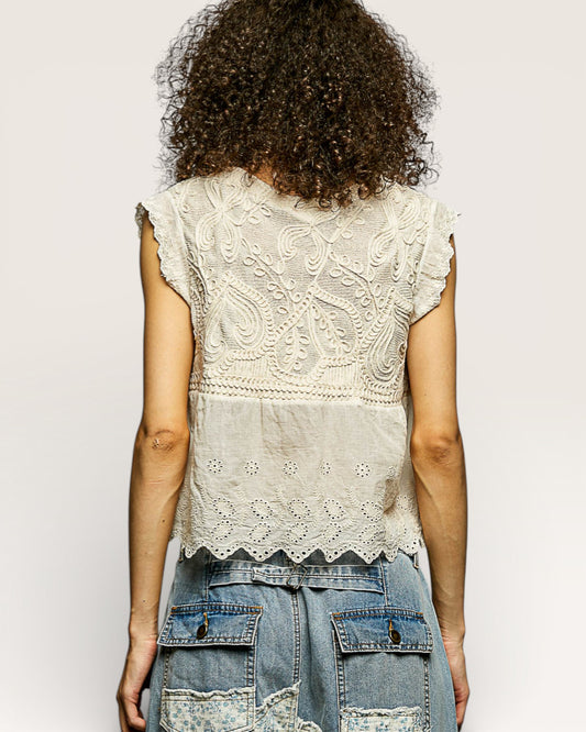 Person wearing a sleeveless embroidered top and denim shorts on a plain background