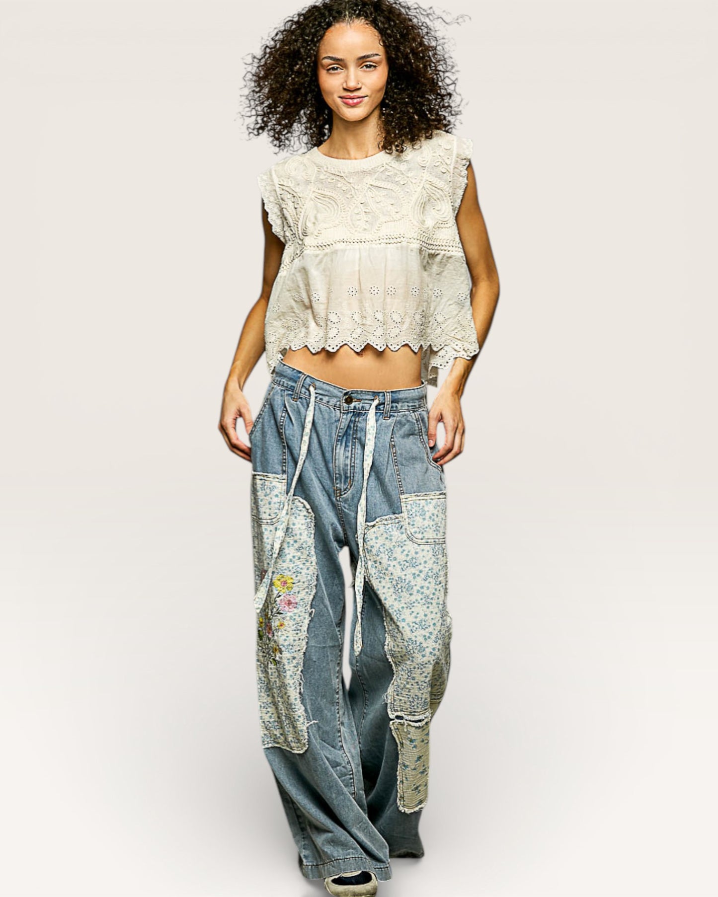 Woman wearing a white lace top and patchwork jeans on a plain background