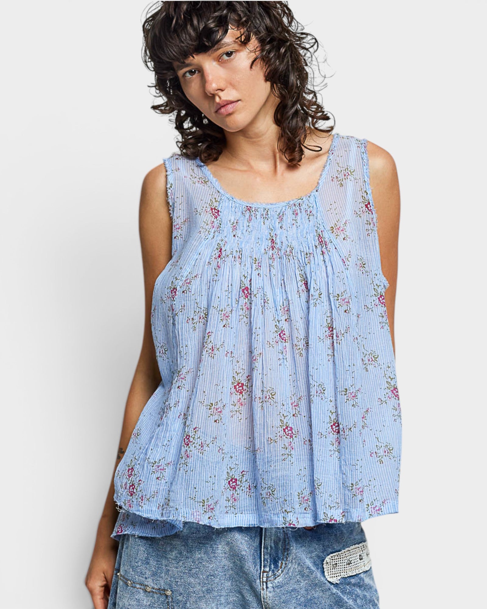 Woman wearing a light blue floral sleeveless top against a white background