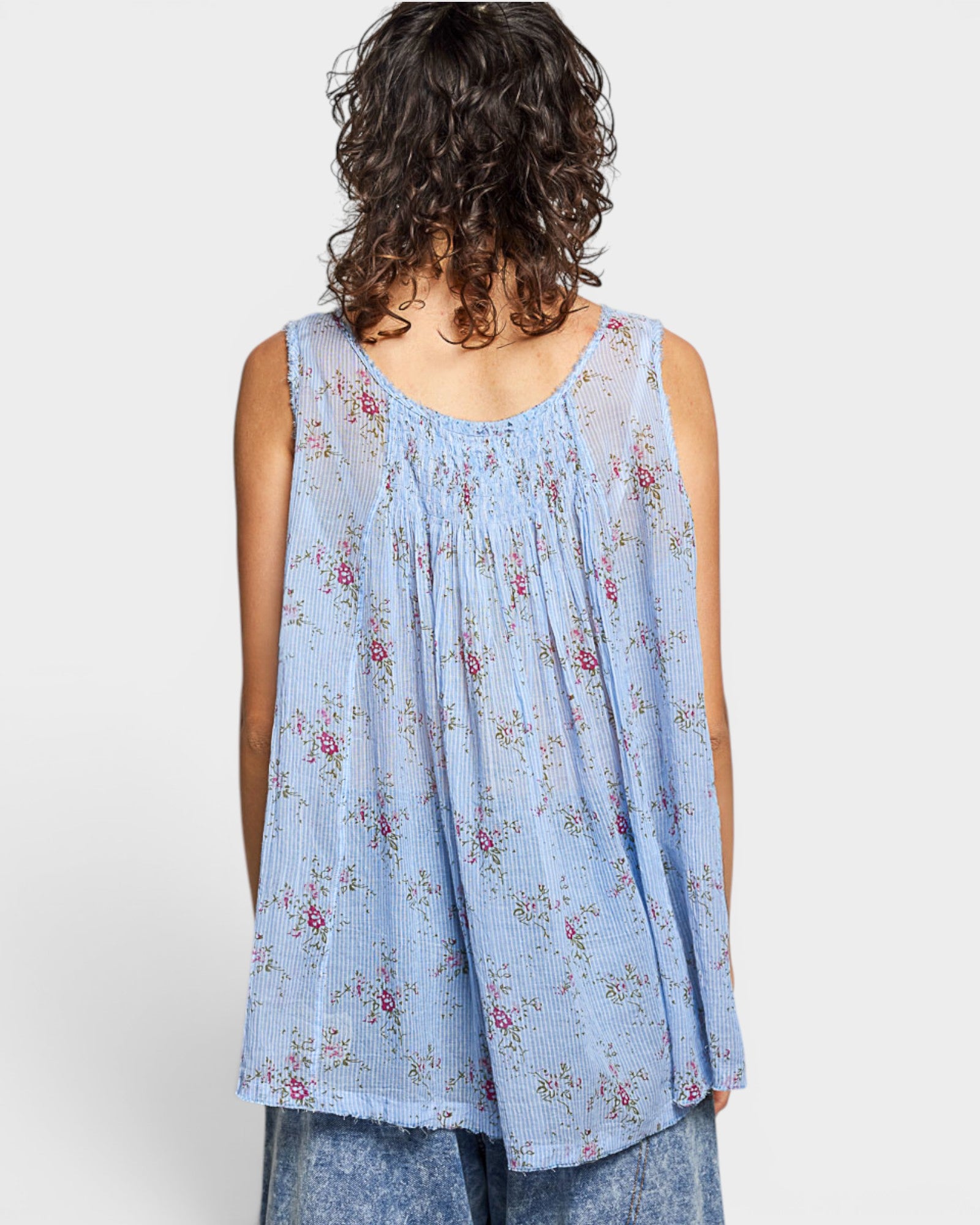 Woman wearing a light blue floral sleeveless top against a white background