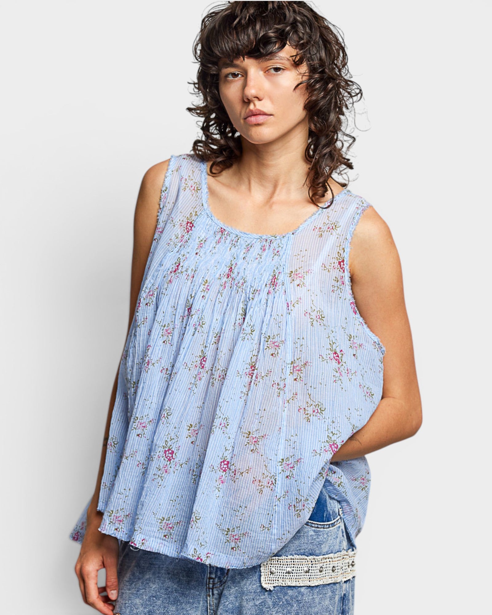 Woman wearing a light blue floral sleeveless top against a white background