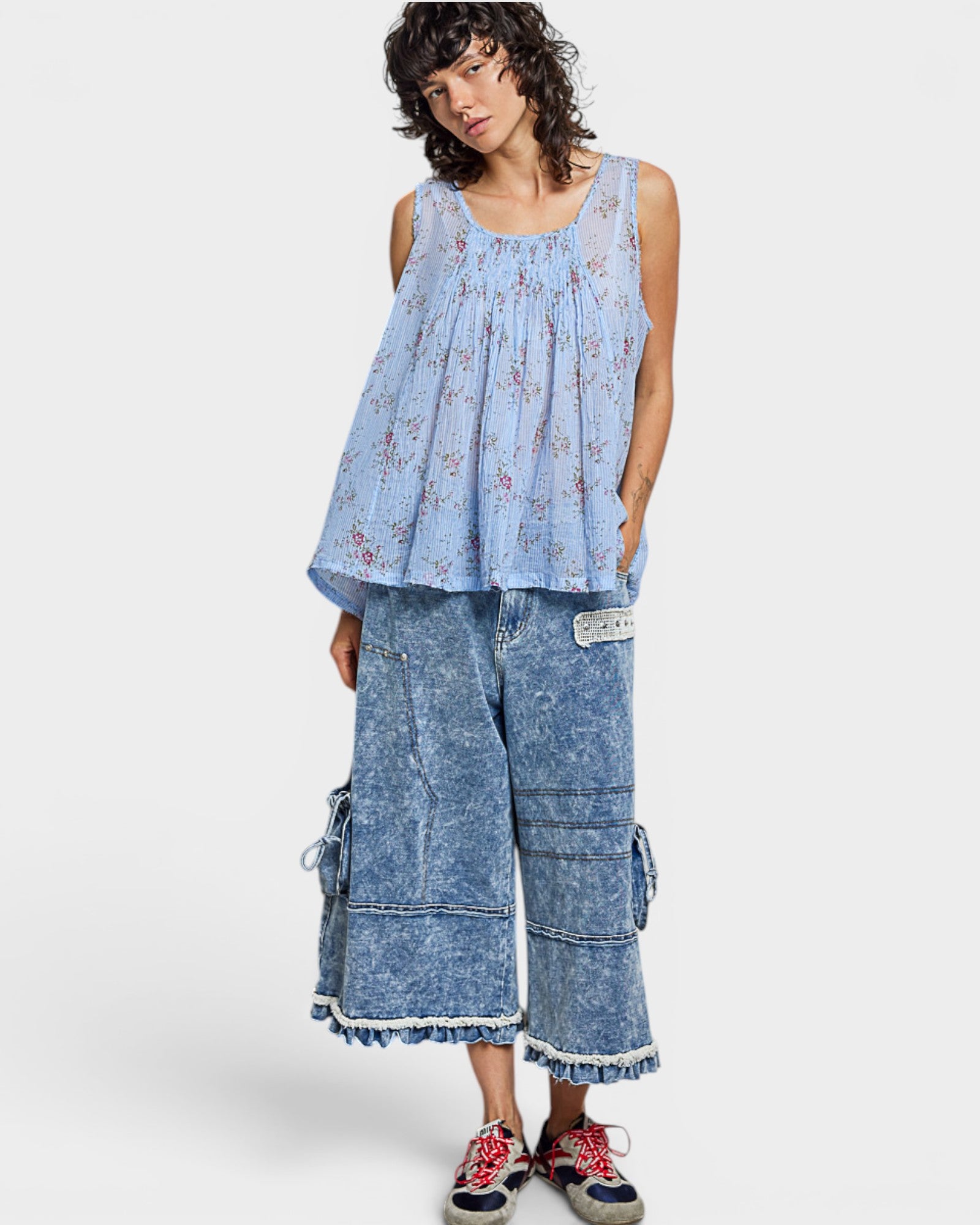 Woman wearing a blue floral top and denim pants on a white background