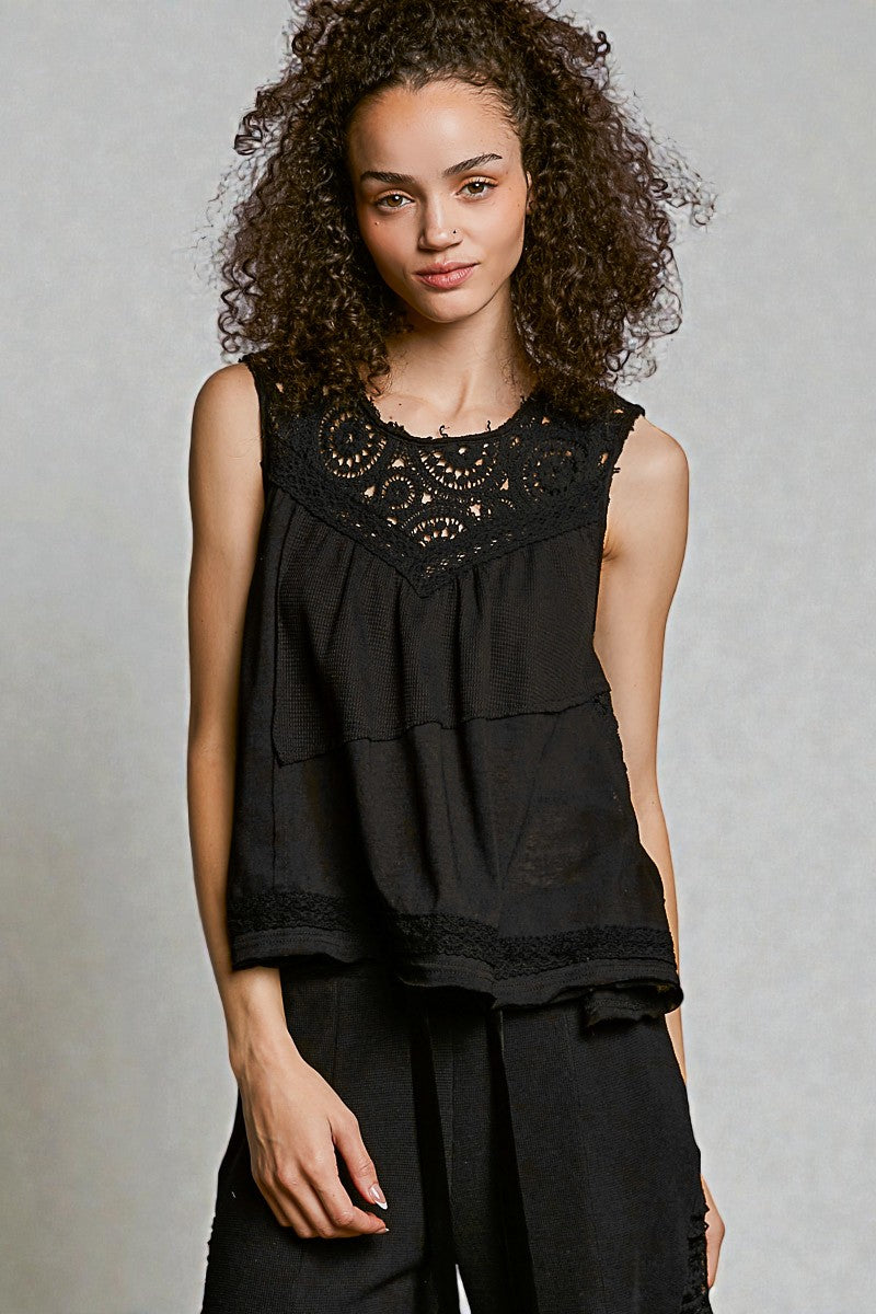 Woman wearing a black sleeveless top with lace details against a plain background