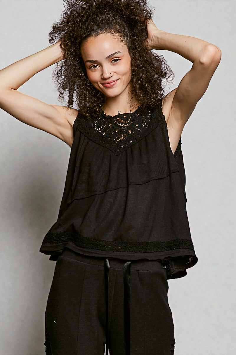 Woman wearing a black sleeveless top with intricate details against a plain background