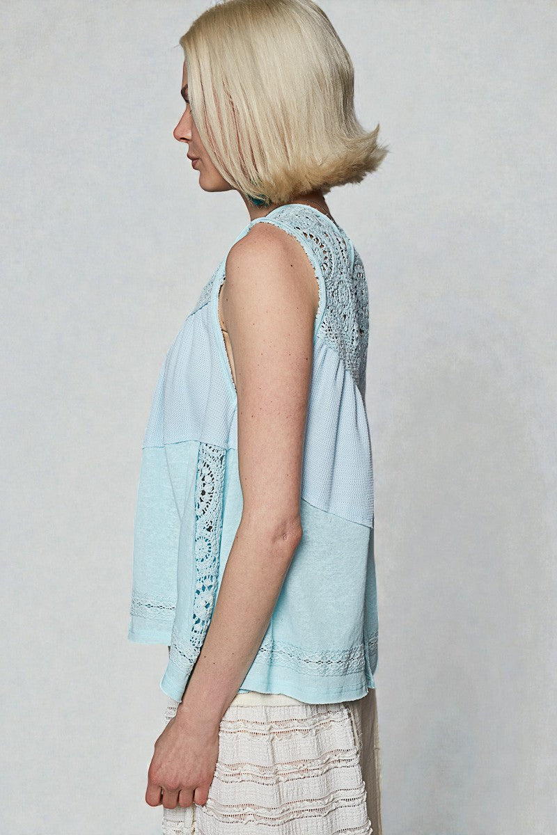 Woman wearing a light blue sleeveless top with lace details on a plain background