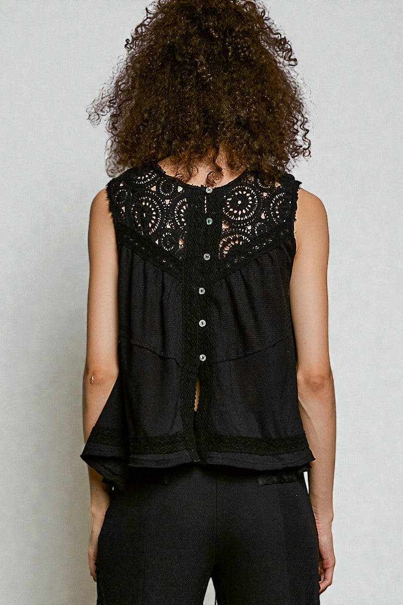 Person wearing a black sleeveless top with intricate detailing on a plain background