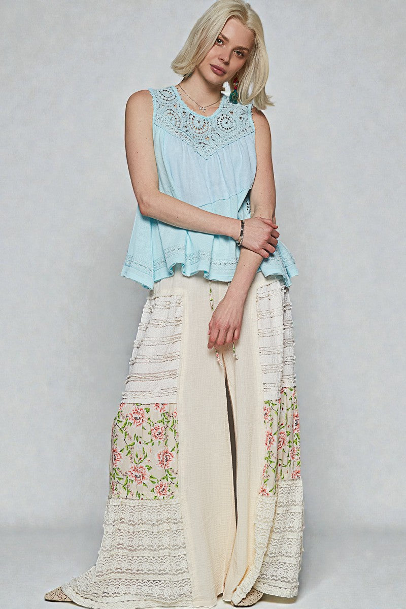 Woman wearing a light blue sleeveless top and a long, floral-patterned skirt on a plain background