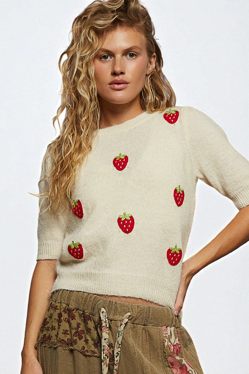 Woman wearing a cream sweater with red strawberry patterns on a white background