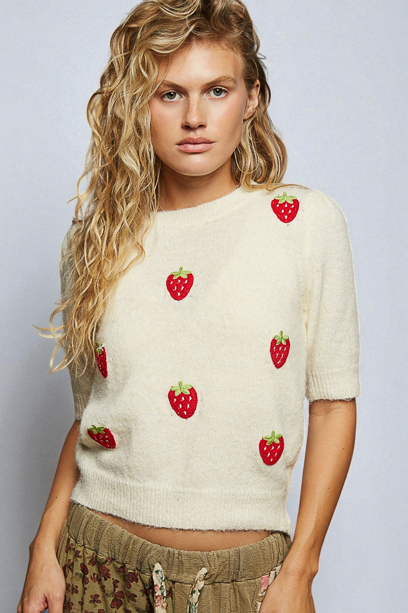 Woman wearing a cream sweater with strawberry patterns on a plain background