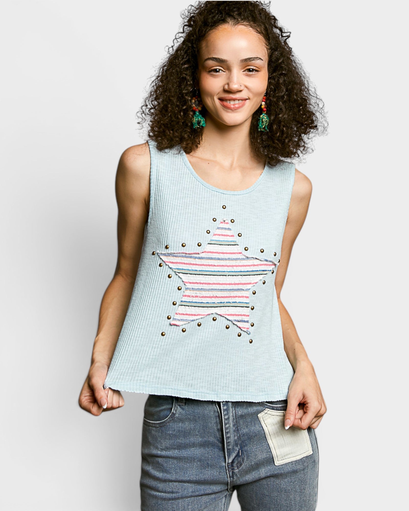 Woman wearing a light blue sleeveless top with star design and jeans on a plain background