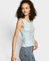 Woman wearing a light blue sleeveless top with decorative buttons and jeans on a white background