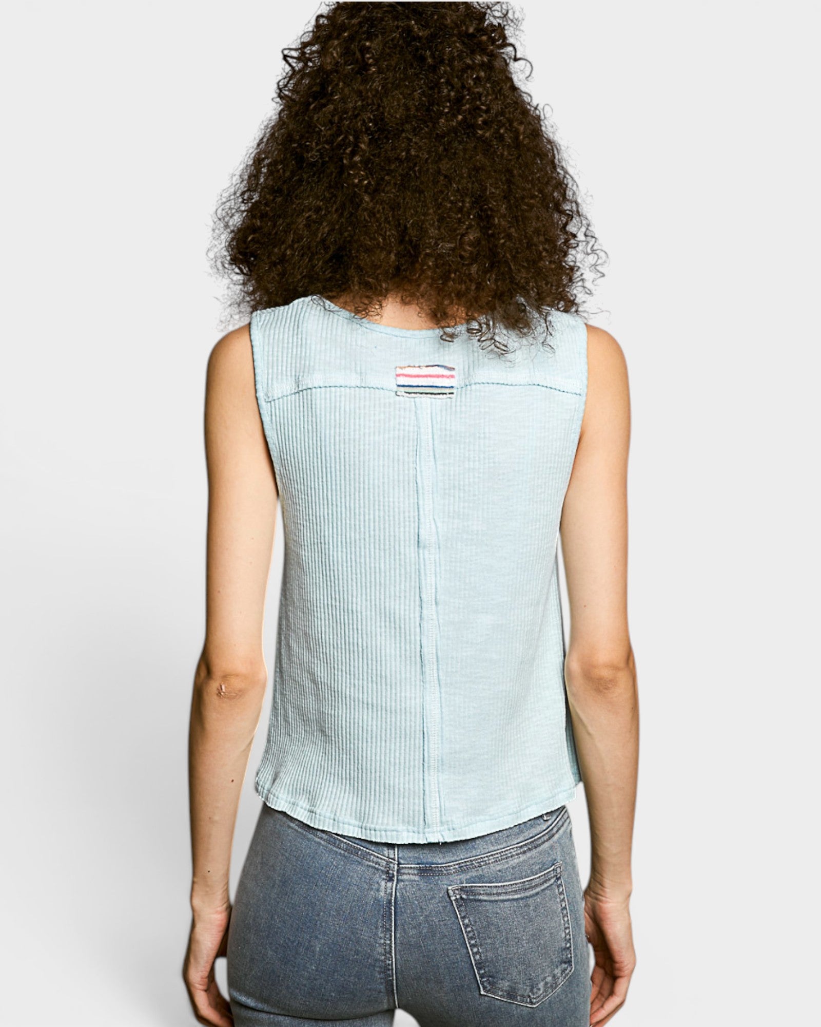Person wearing a light blue sleeveless top with a small red and white logo on a plain background