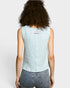 Person wearing a light blue sleeveless top with a small red and white logo on a plain background