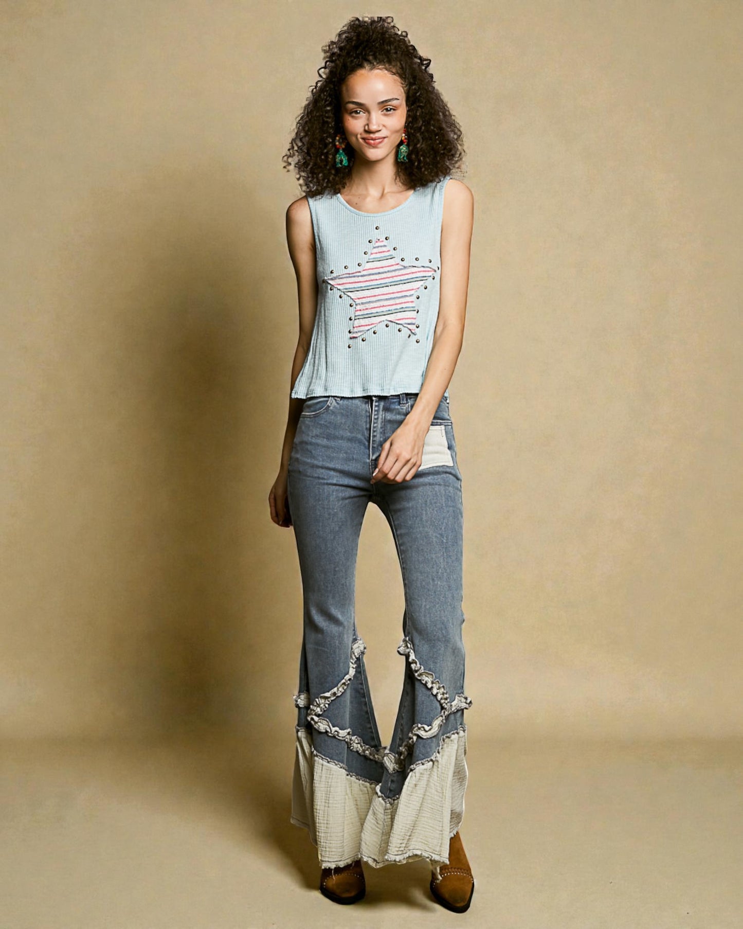 Woman wearing a light blue sleeveless top with a graphic design and high-waisted jeans with lace details on a beige background.