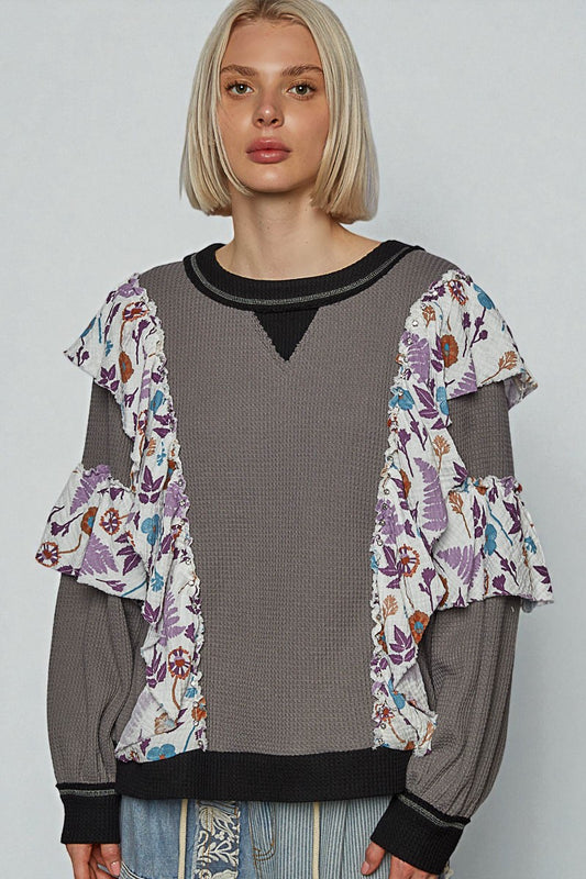 Woman wearing a gray sweater with floral sleeves against a plain background