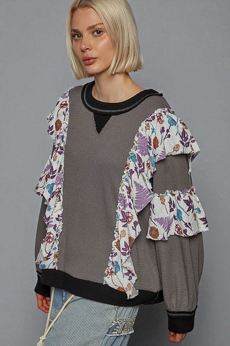 Woman wearing a layered outfit with a floral cardigan over a gray top and pants on a gray background