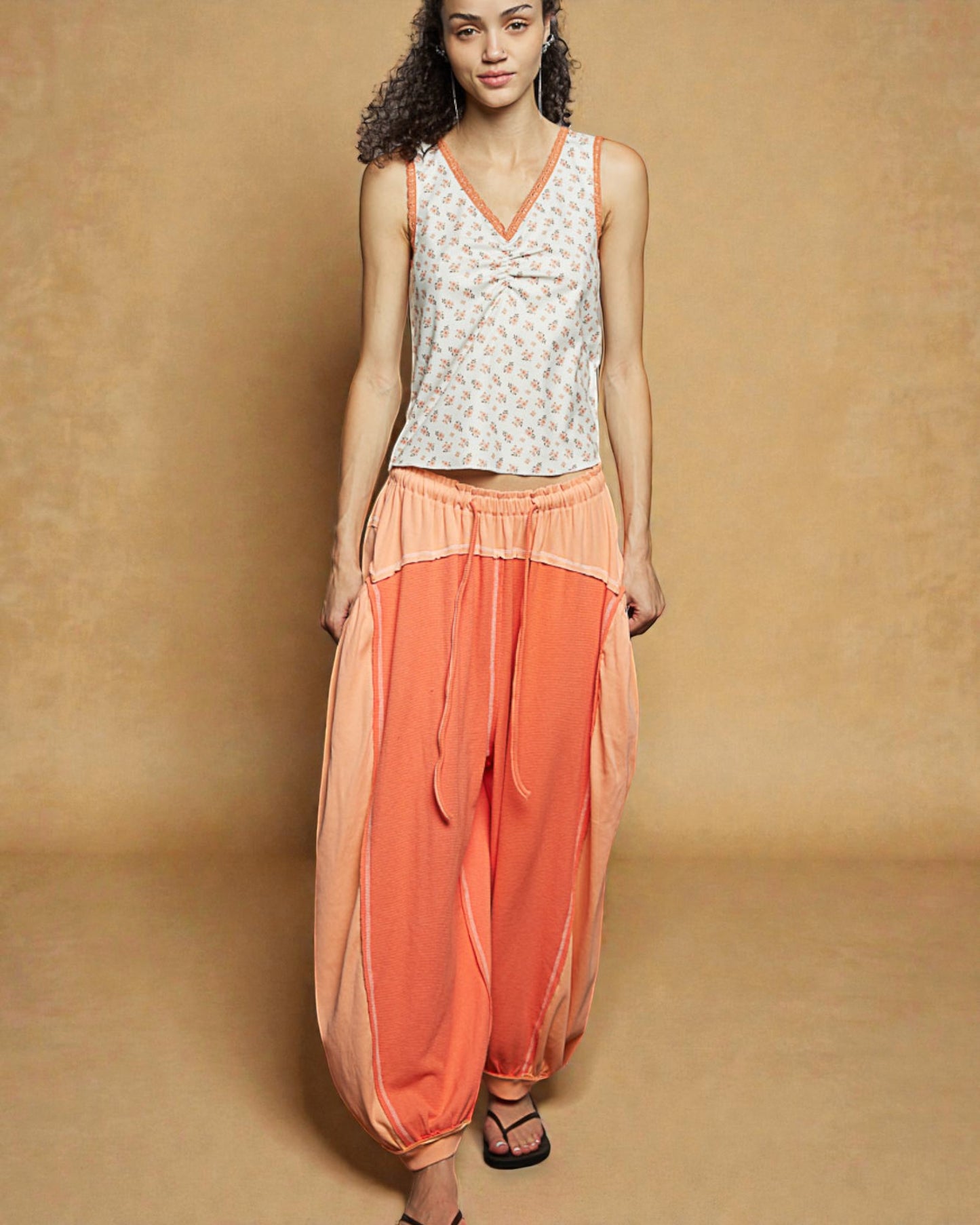 Woman wearing a sleeveless top and orange pants against a beige background
