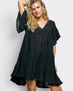 Woman wearing a black tiered dress against a plain background
