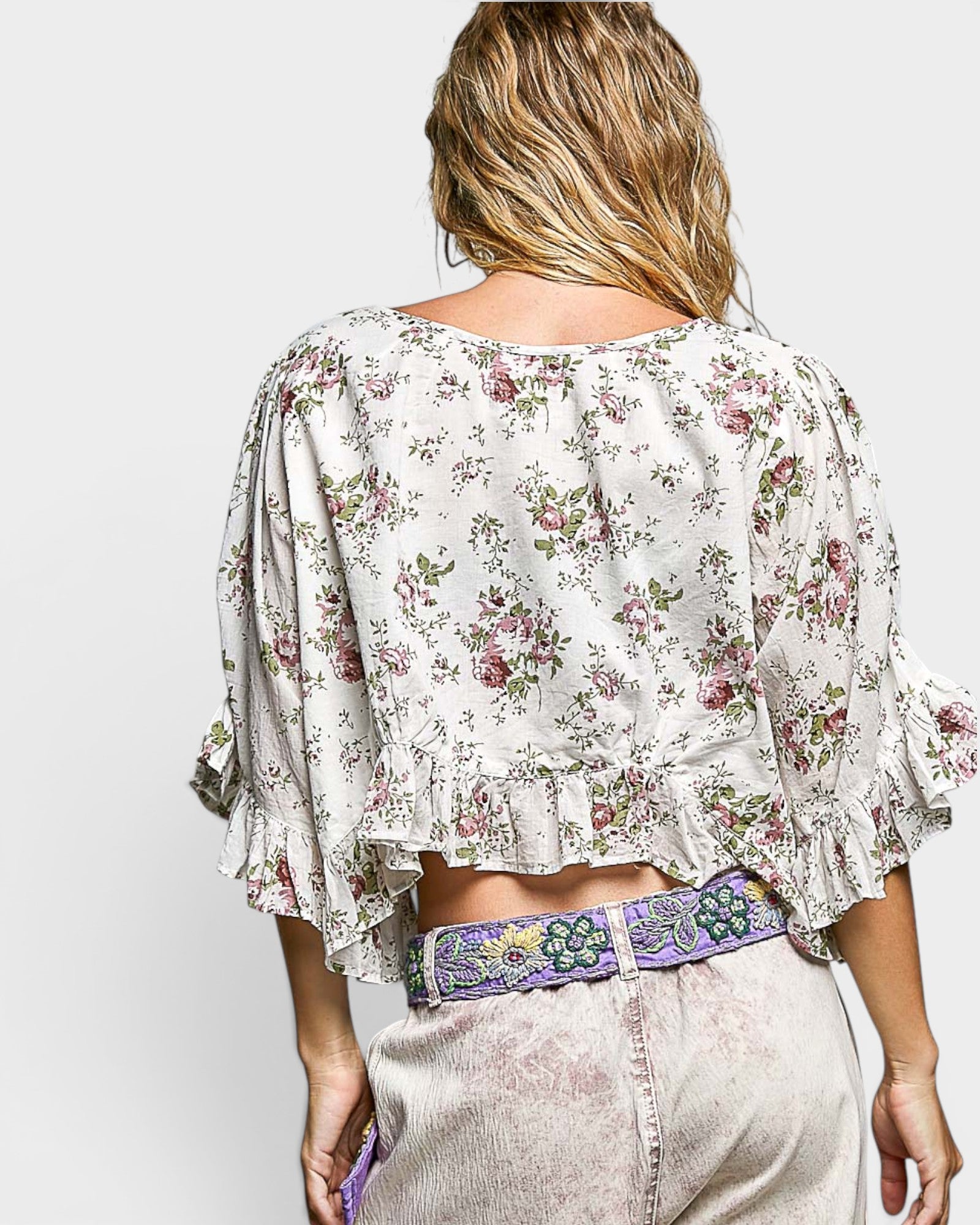 Woman wearing a floral blouse and light pants with a colorful belt on a white background