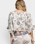 Woman wearing a floral blouse and light pants with a colorful belt on a white background