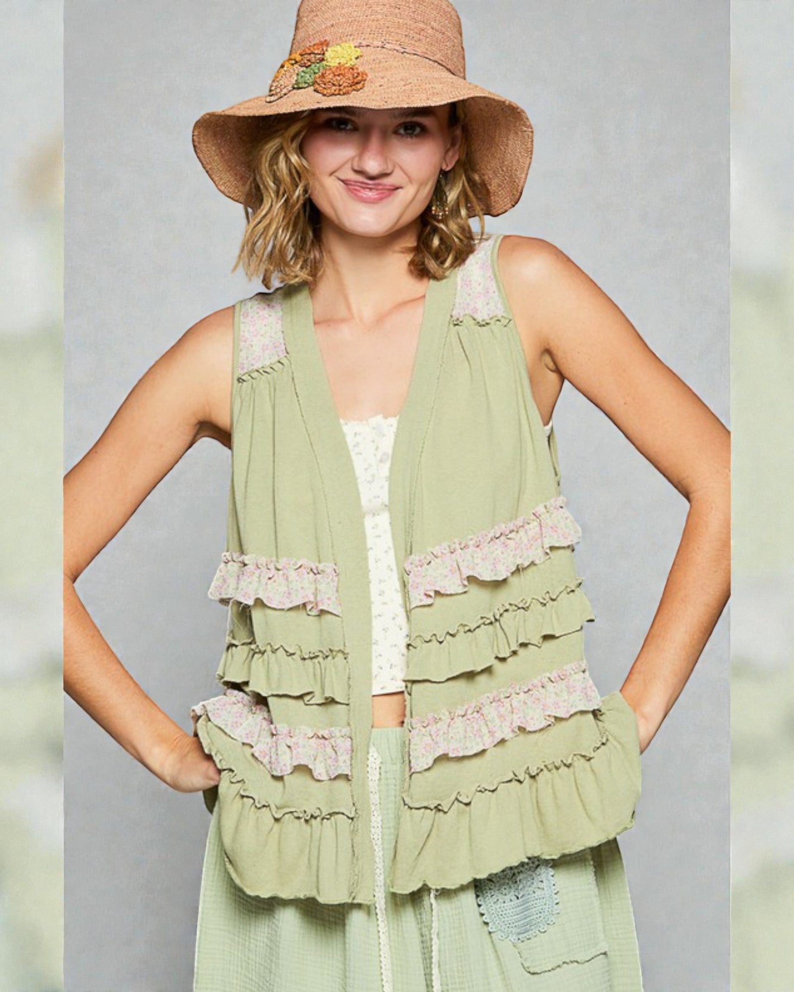 Woman wearing a green layered dress with lace details and a straw hat on a gray background