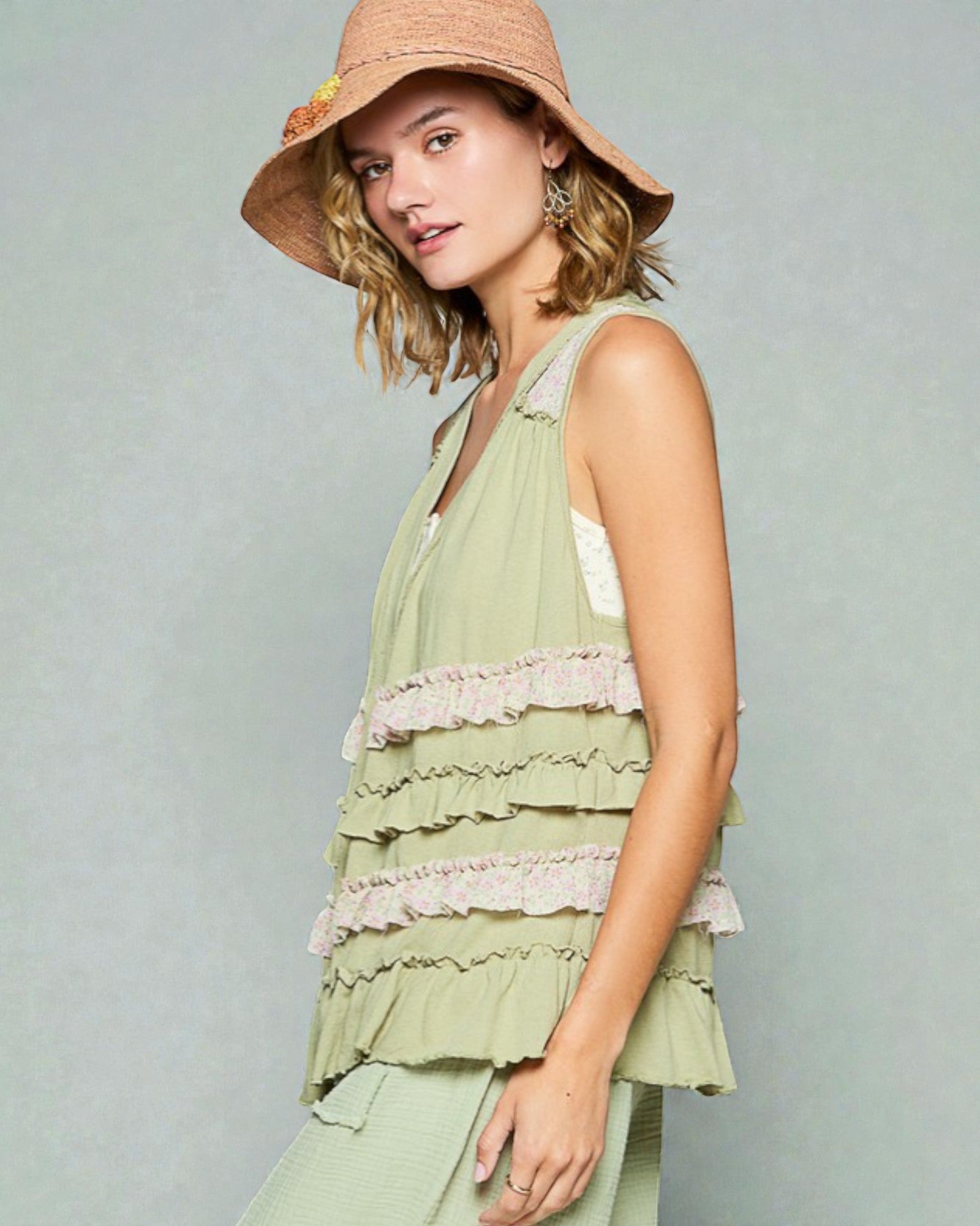Woman wearing a light green layered dress and straw hat on a plain background